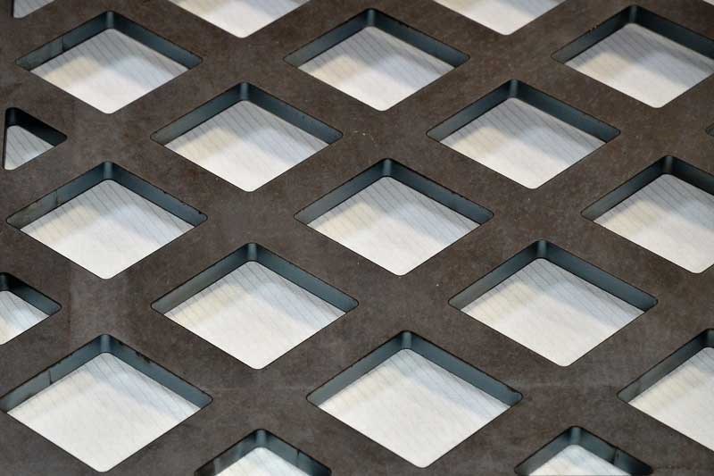 Svart metallgaller med kvadratiska hål och pappersunderlag.